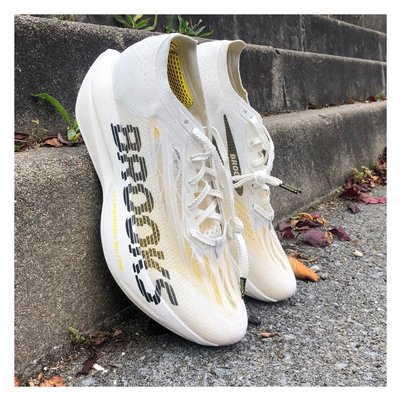 Paire de Brooks Hyperion Elite 6 posée contre une marche, vue 3/4 face, coloris blanc et jaune