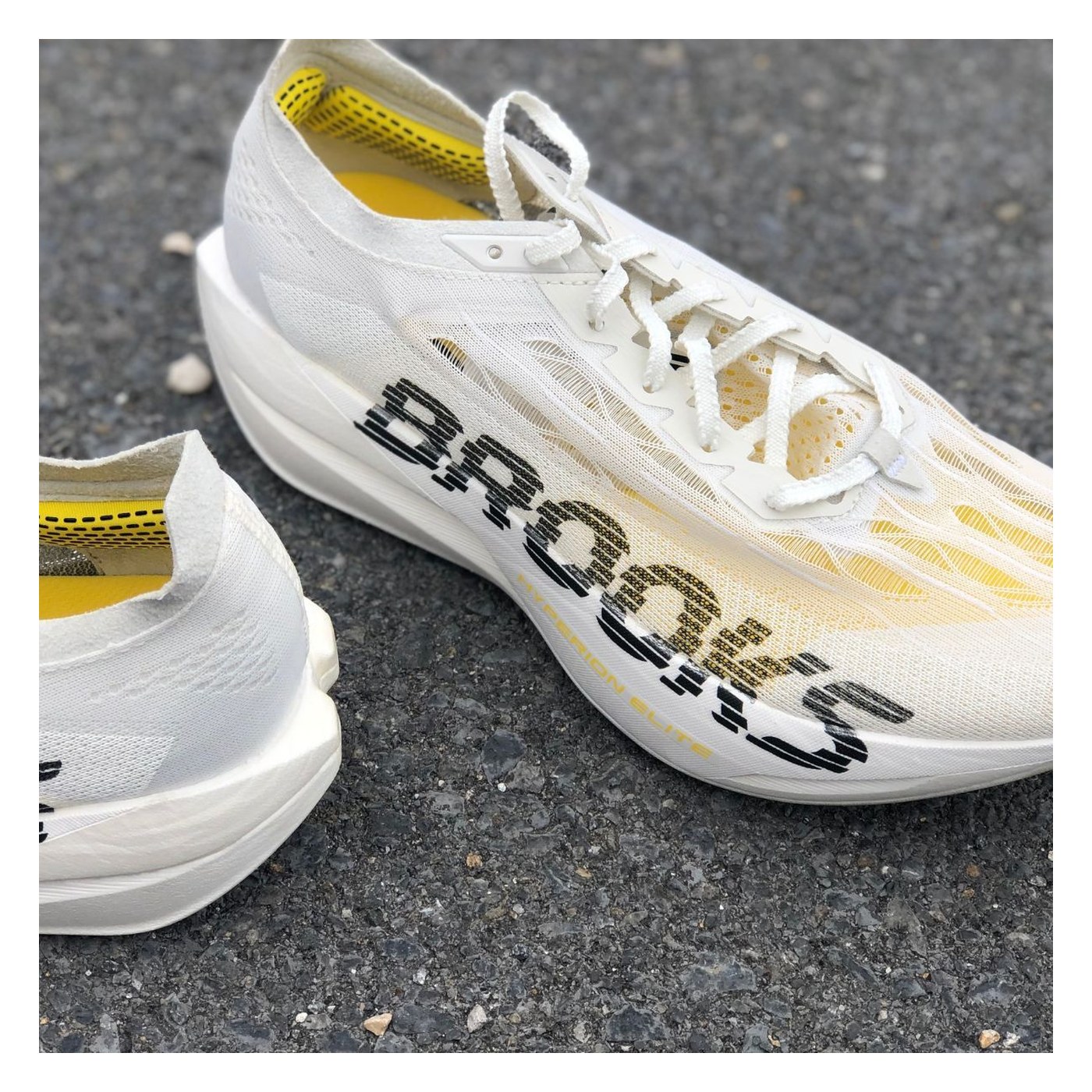 Paire de Brooks Hyperion Elite 6 sur bitume, vue 3/4 face, tige TPU et accents jaunes visibles